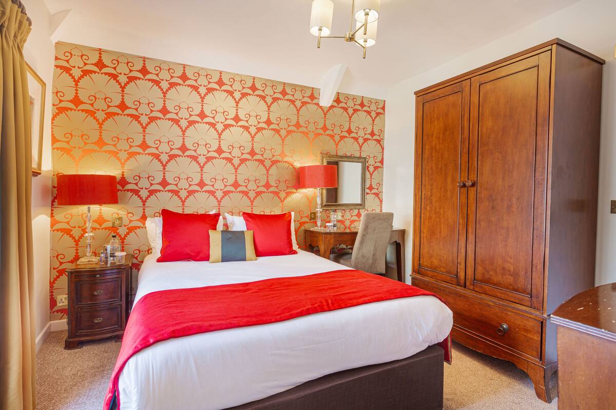 A hotel room with a large bed, a wardrobe, a nightstand, and a mirror.