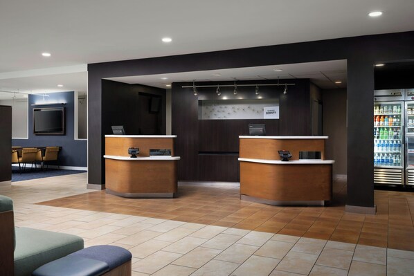 A reception area with two counters, a seating area with chairs, and a refrigerator stocked with beverages.