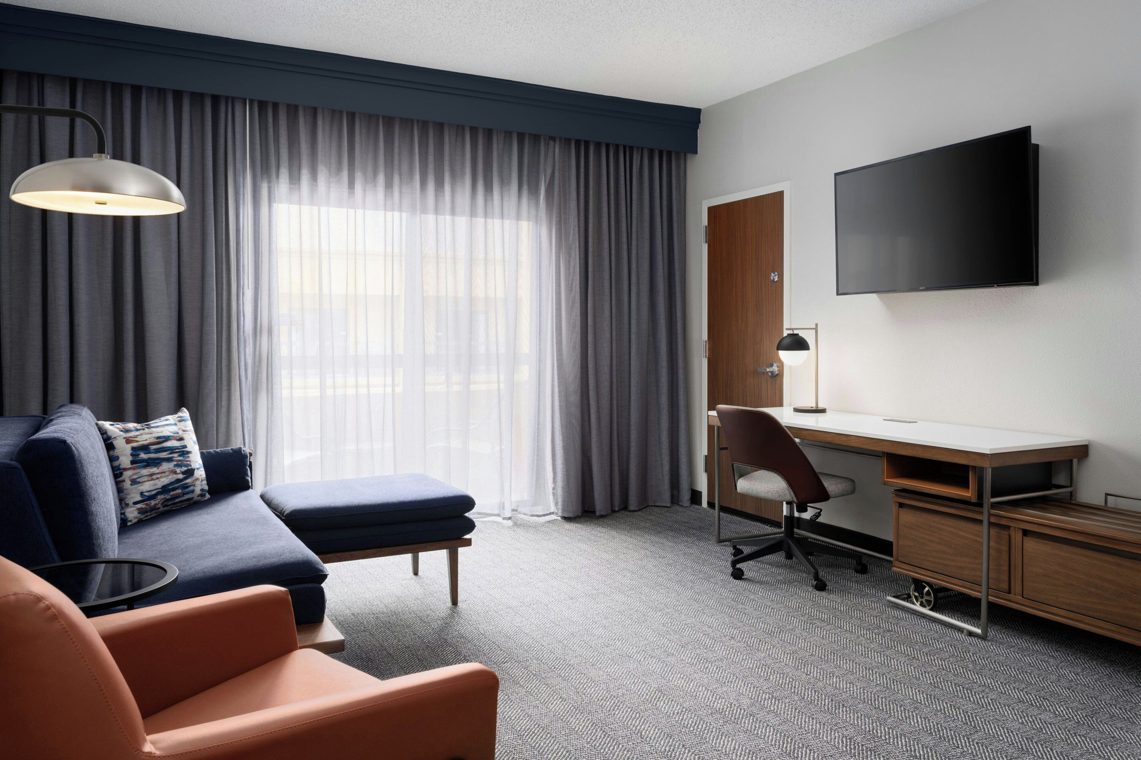 A modern hotel room with a sofa, a desk, and a TV.