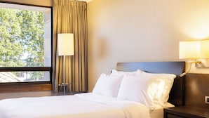 Habitación de hotel con una cama grande, dos lámparas de noche, una ventana con cortinas y vistas a árboles.