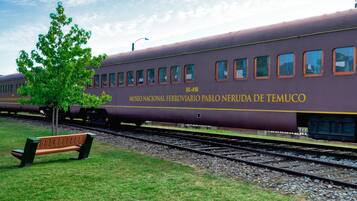 A train with "MUSEO NACIONAL FERROVIARIO PABLO NERUDA DE TEMUCO" written on its side, parked on tracks with a bench and a tree nearby.