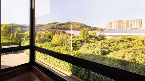 A view from a window with a metal frame, overlooking a parking lot, dense greenery, and a building with a red roof. - Holiday Inn Express Temuco by IHG (Temuco)