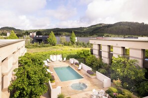 A rooftop pool area with a hot tub, lounge chairs, and a view of a forested hill.