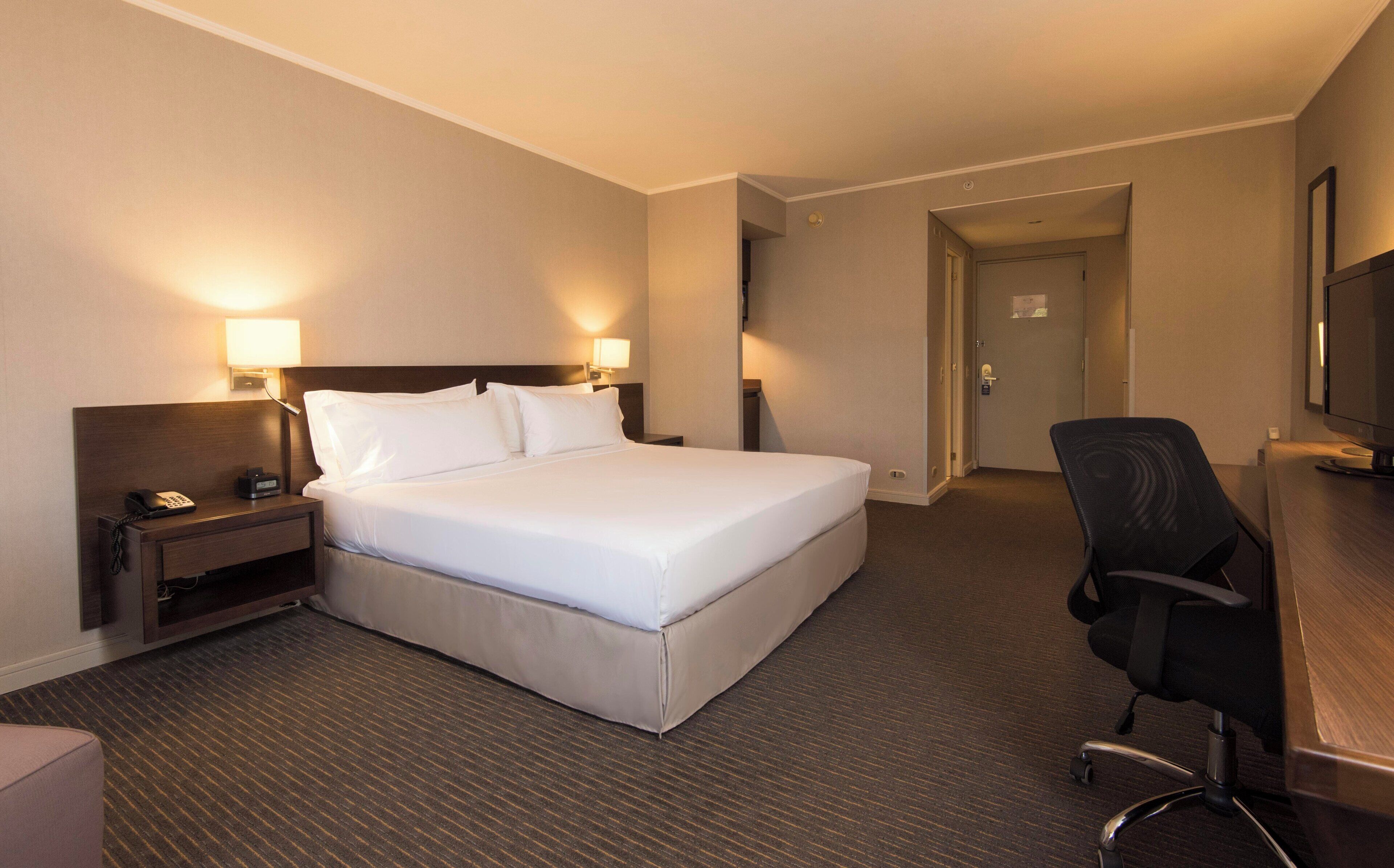 Una habitación de hotel con una cama grande, lámparas de noche, un escritorio con computadora y una silla.