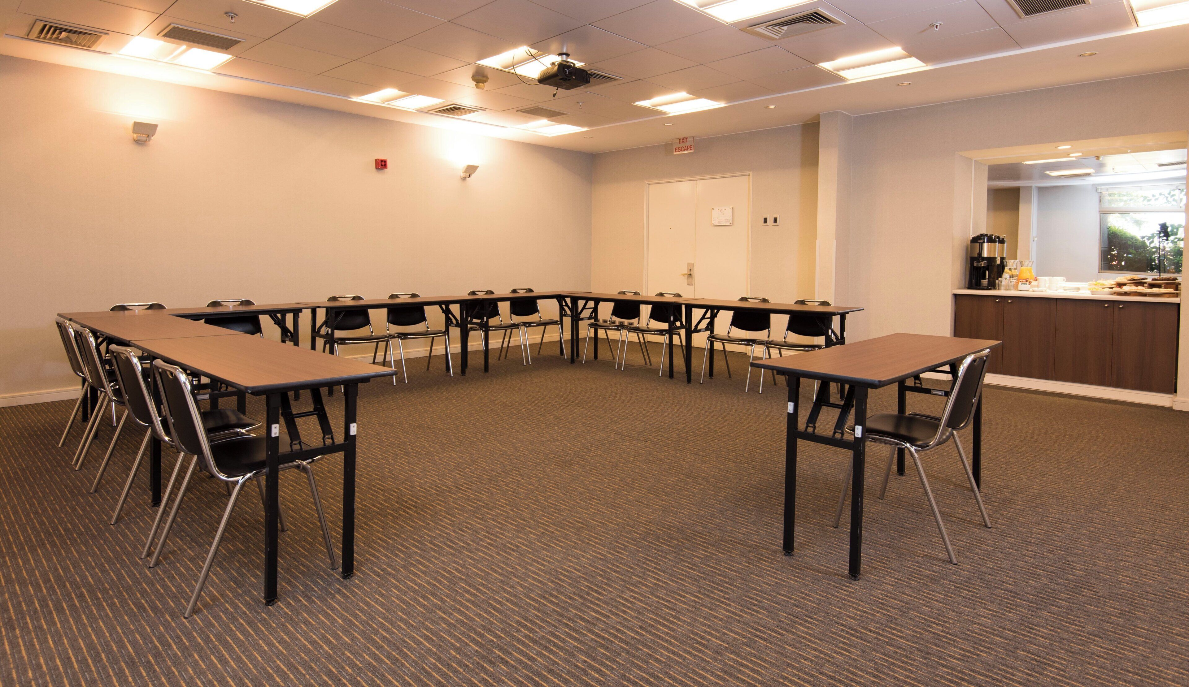 A conference room with a U-shaped table, chairs, a whiteboard, and a kitchenette area.