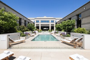 A modern hotel with a central pool, sun loungers, and a clear blue sky.