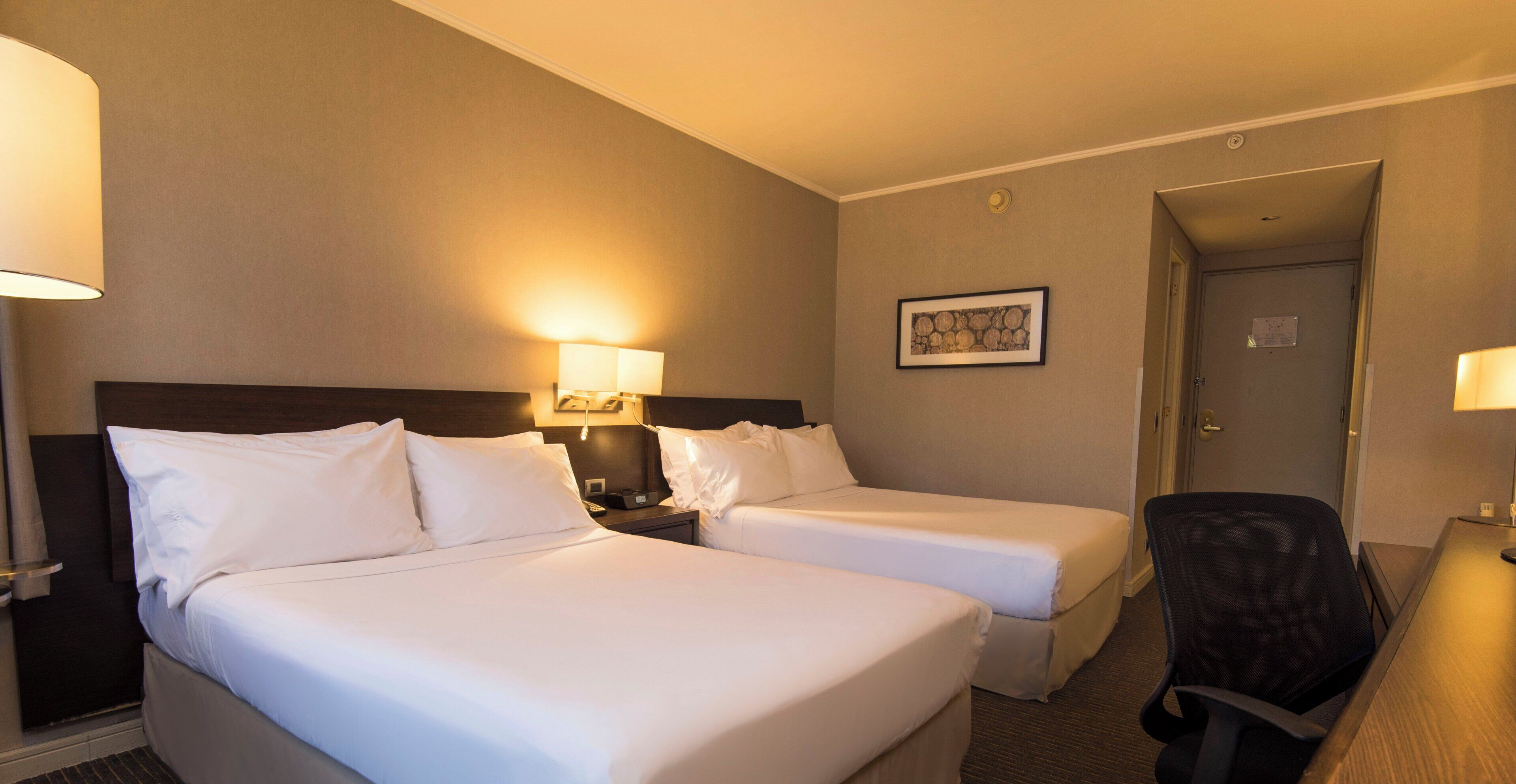 A hotel room with two beds, a desk, and a chair.