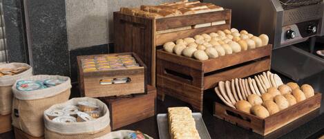 Uma bancada de cozinha com diversos pães e produtos de panificação expostos em caixas e cestos de madeira.