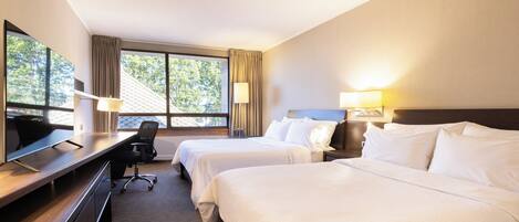 Quarto de hotel com duas camas, uma escrivaninha, uma cadeira e uma televisão.