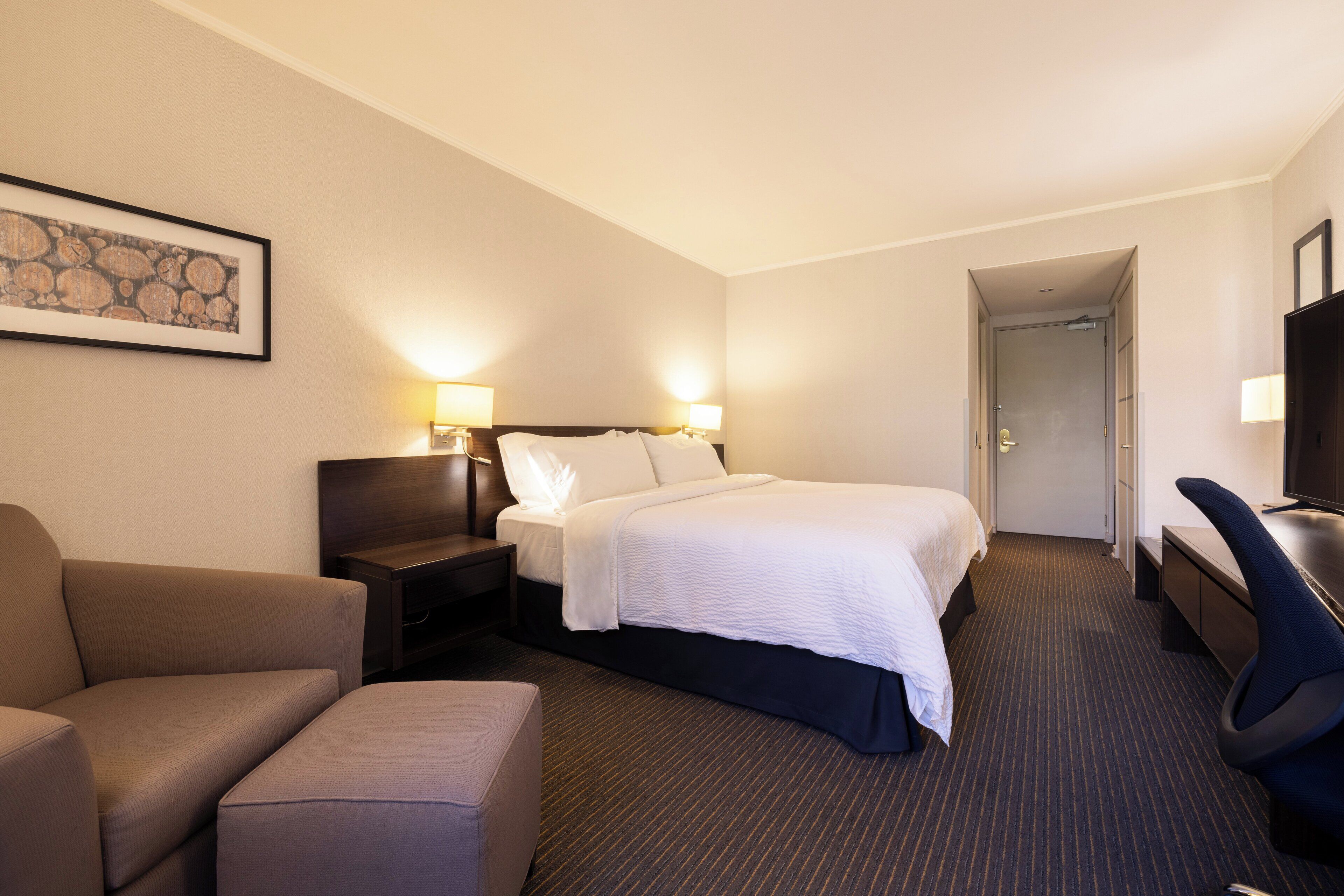 Ein Hotelzimmer mit einem Bett, einem Schreibtisch, einem Sessel und einem Fernseher.