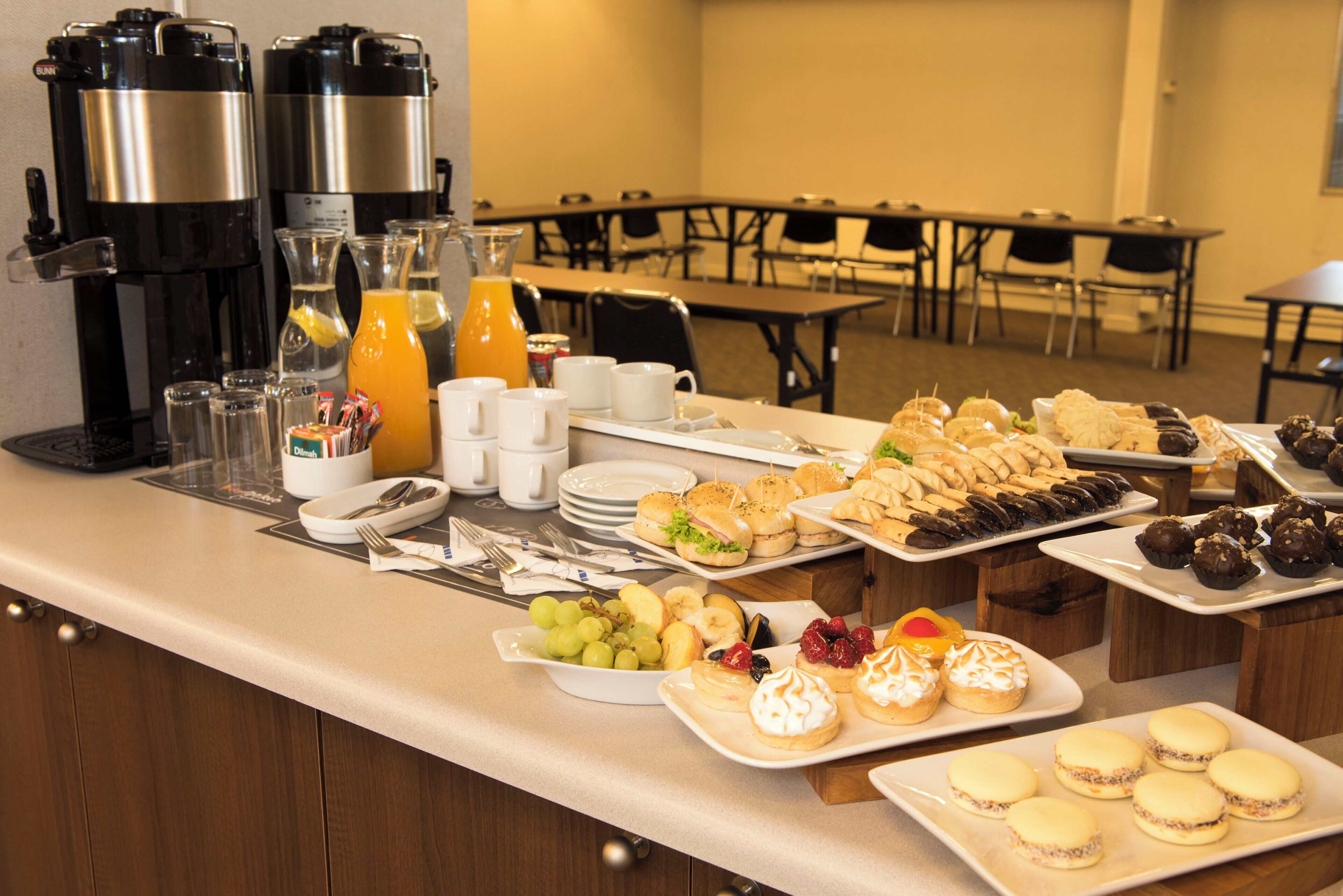 Ein reichhaltiges Buffet mit verschiedenen Speisen, darunter Sandwiches, Gebäck und Früchte, sowie Kaffee- und Saftautomaten.