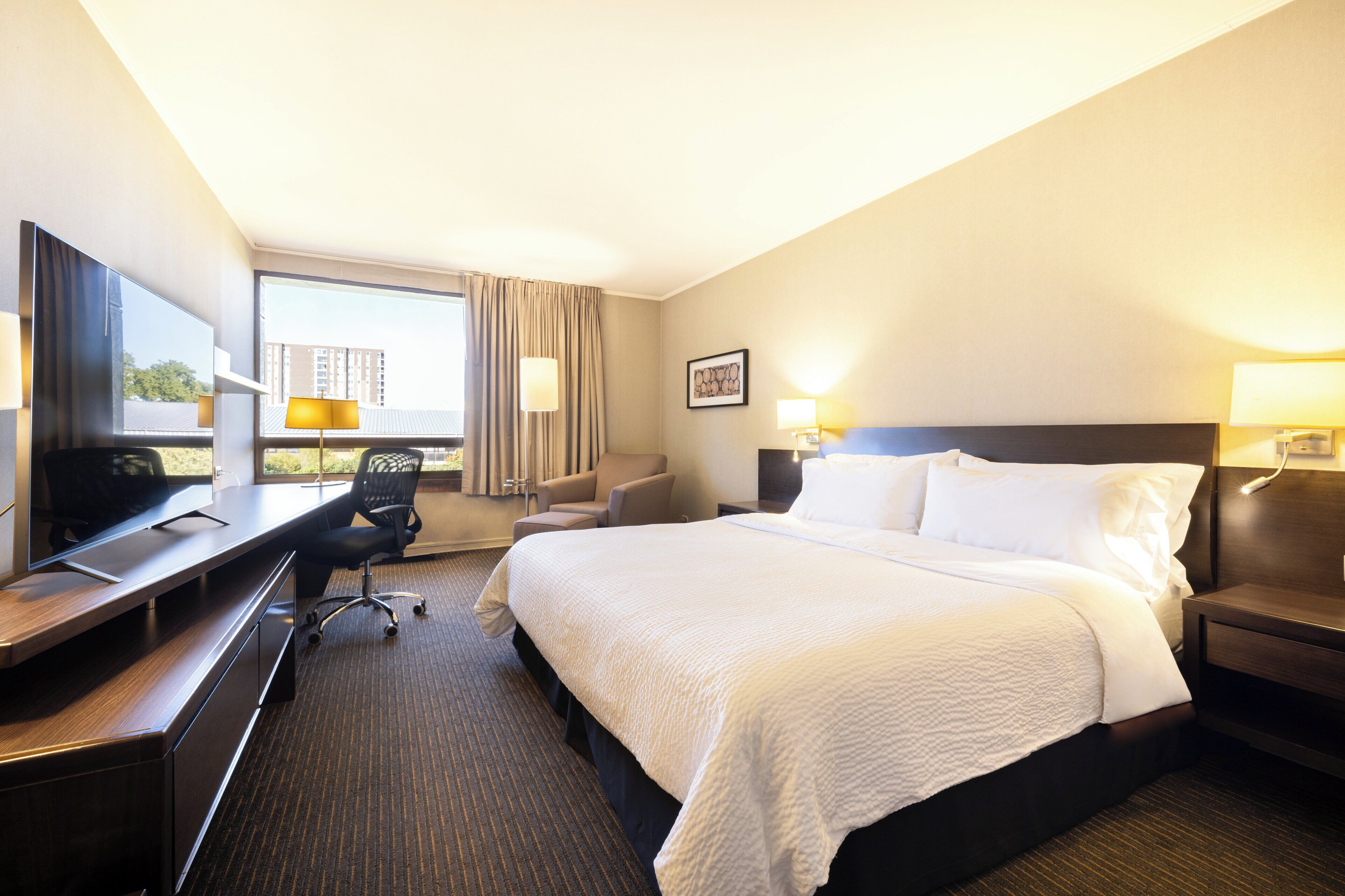 A hotel room with a bed, desk, chair, and a television.