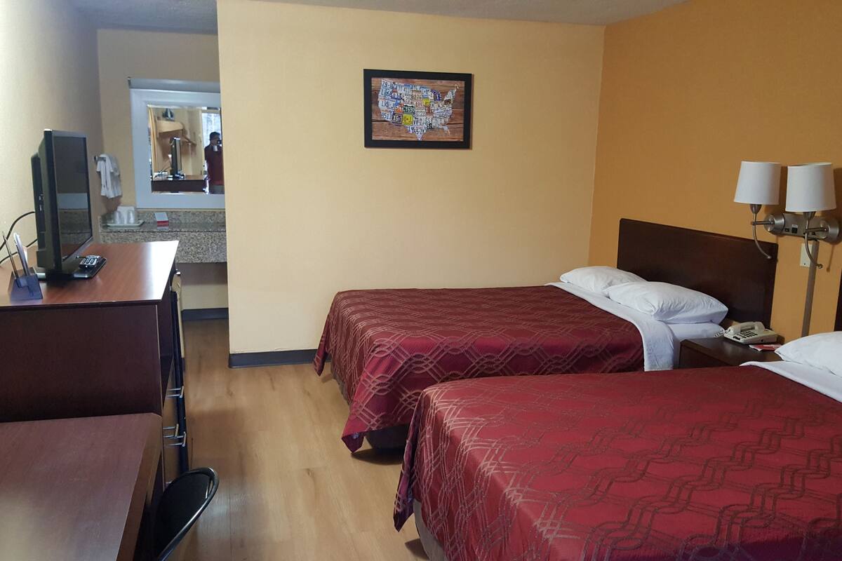 Une chambre d’hôtel avec deux lits, un bureau, une télévision et une salle de bain visible à travers une porte ouverte.