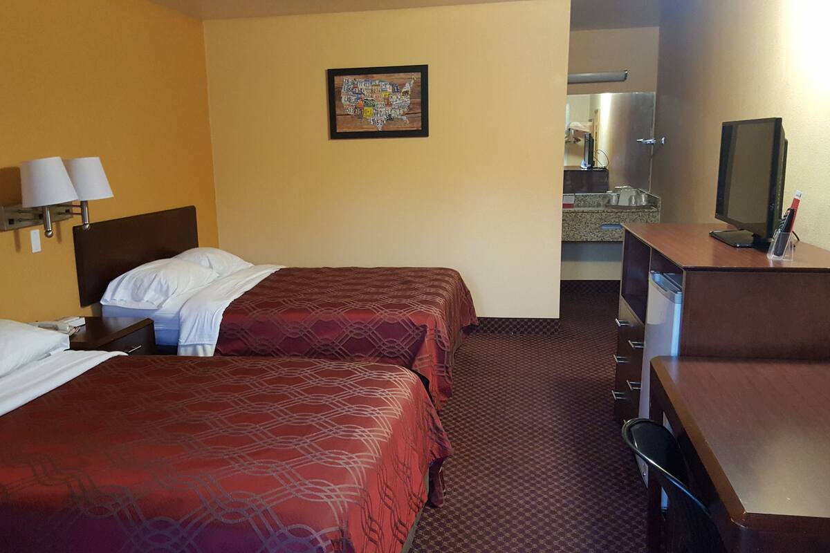Une chambre d’hôtel avec deux lits, un bureau, une télévision et une salle de bain visible au fond.