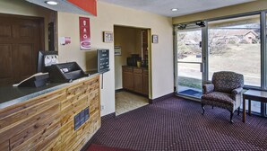 A reception area with a wooden counter, a reception desk, a chair, and a view of the outside through a glass door. - Econo Lodge Near Bluefield College (Bluefield)