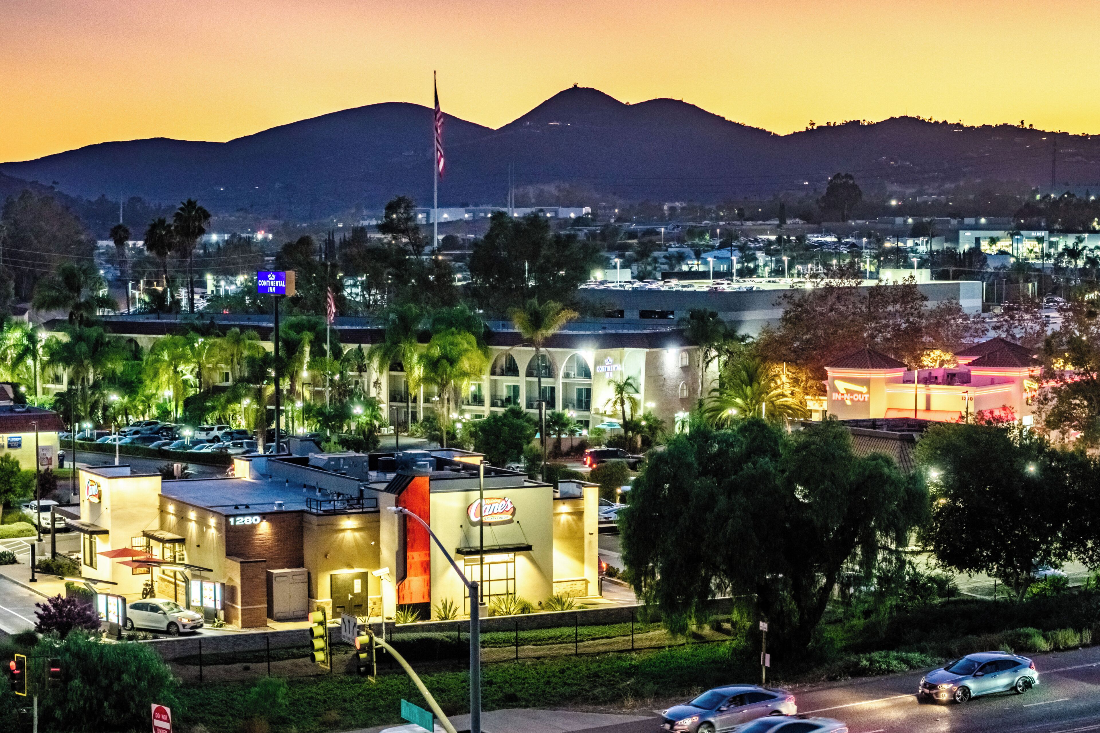 A hotel with a prominent sign, a parking lot, and a view of a cityscape with mountains in the background.