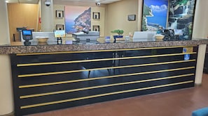 A reception desk with a computer, a clock, and a sign indicating check-out time. - Continental Inn San Diego Hotel Escondido (Escondido)