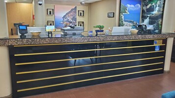A reception desk with a computer, a clock, and a sign indicating check-out time.