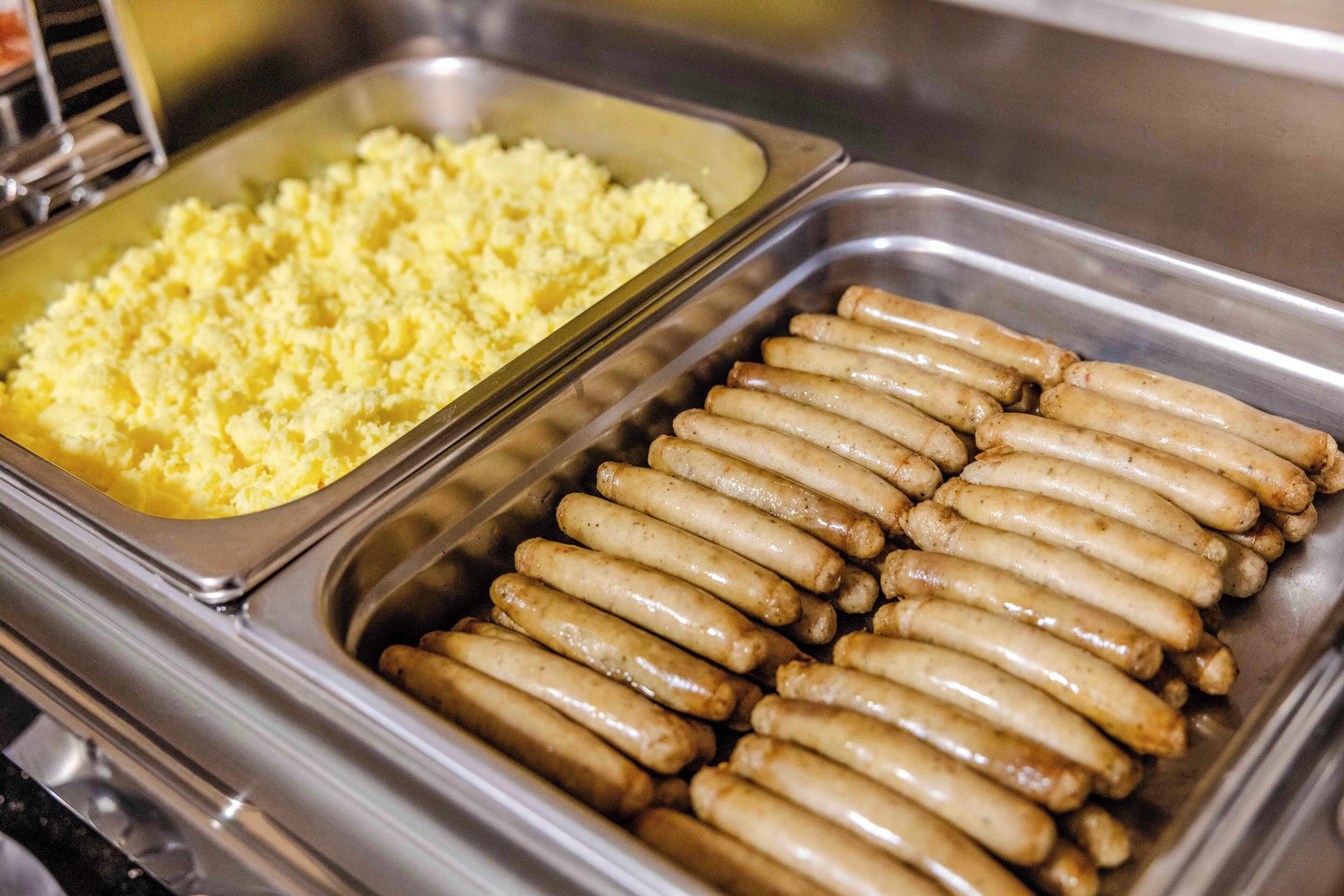 A buffet with two trays, one containing mashed potatoes and the other with grilled sausages.