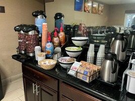 A buffet setup with coffee dispensers, coffee mugs, and food containers.