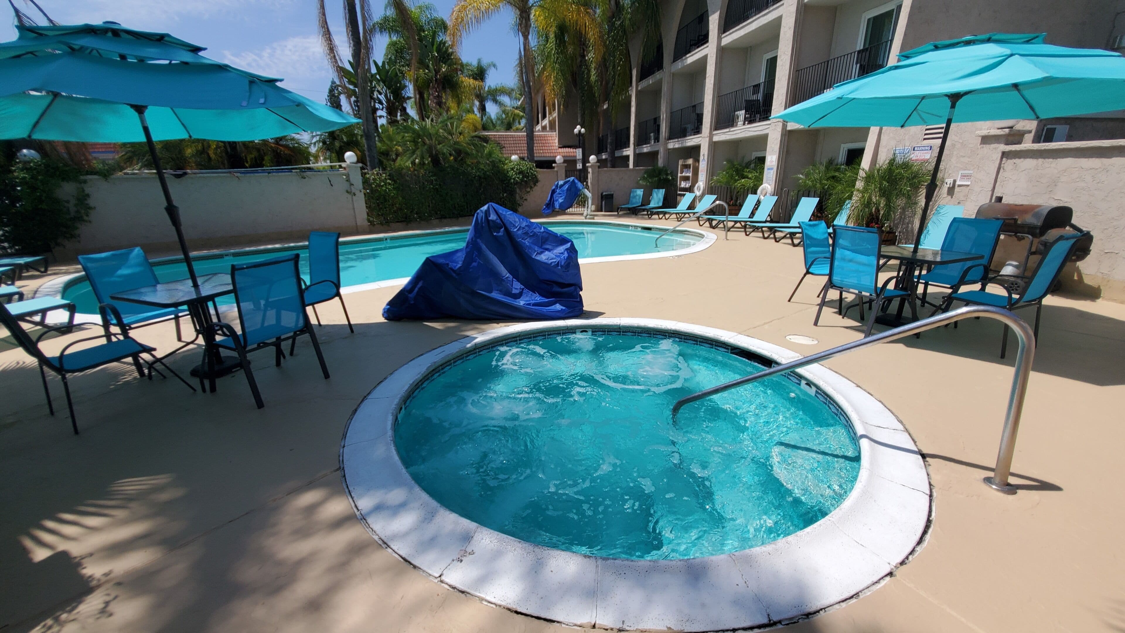 A pool area with lounge chairs and umbrellas, surrounded by a building with balconies.