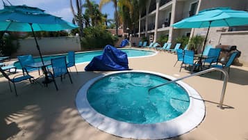 A pool area with lounge chairs and umbrellas, surrounded by a building with balconies.