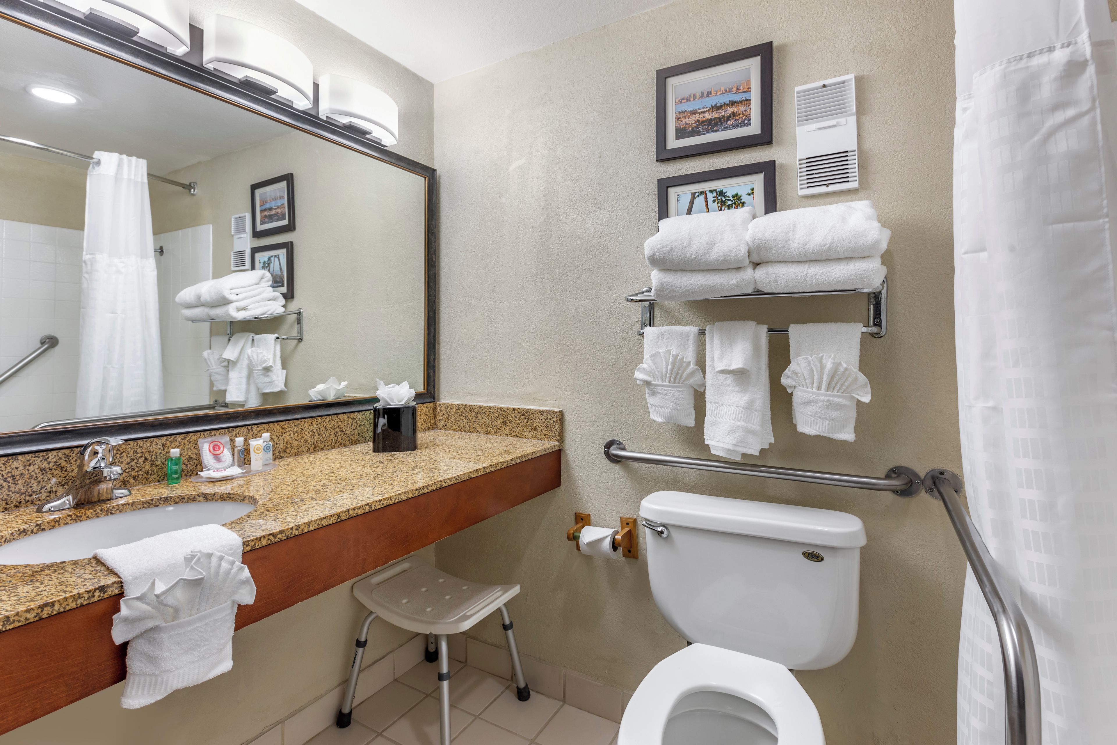 A bathroom with a sink, toilet, and a shower curtain. There are towels and a hand dryer on the wall.