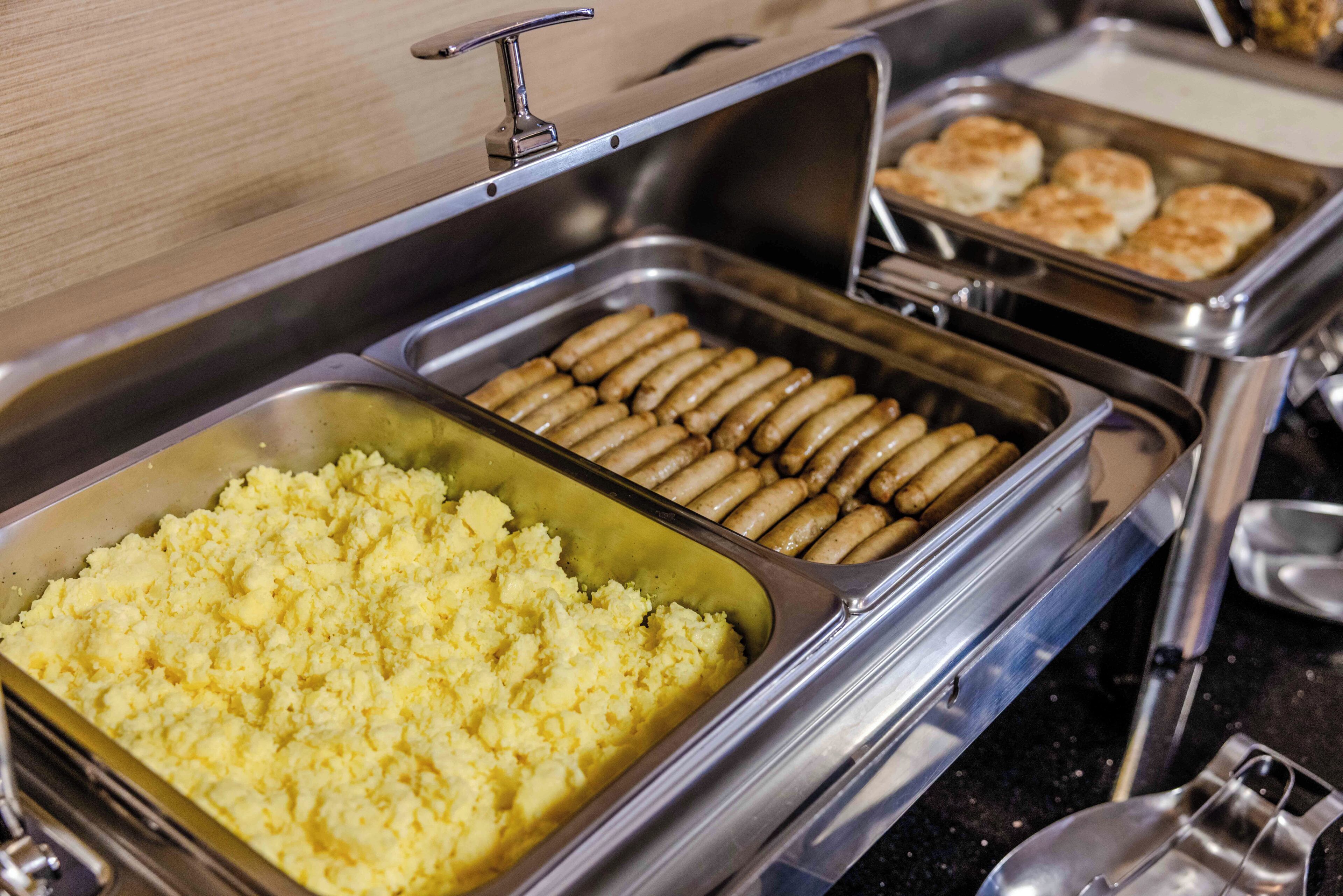 A buffet with various food items including mashed potatoes, sausages, and pastries.