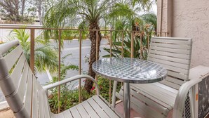 Ein Balkon mit rundem Tisch und zwei Stühlen, umgeben von Grünpflanzen und Blick auf die Straße.