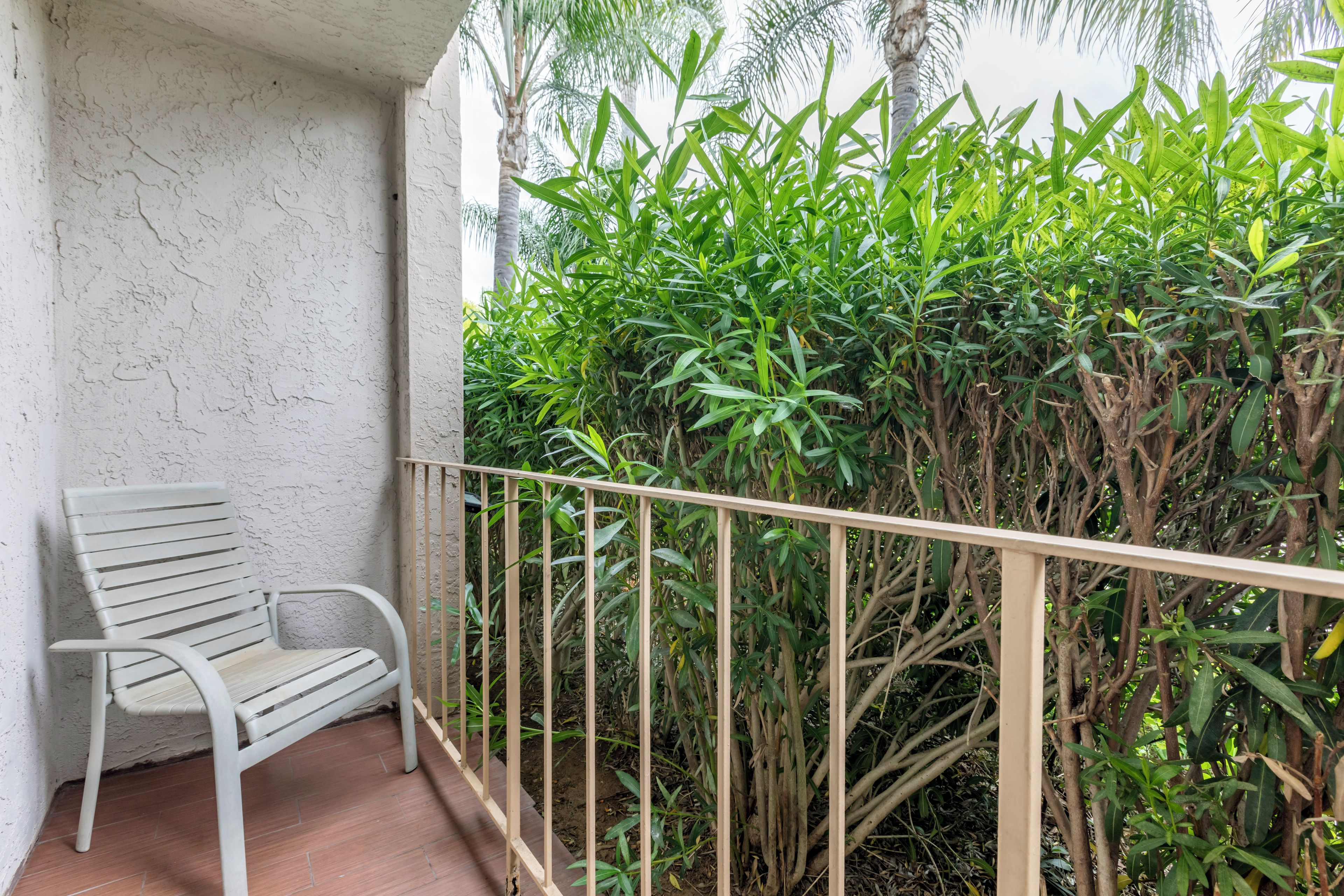 A balcony with a white chair, a metal railing, and dense green foliage in the background.