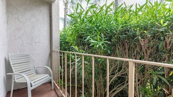 A balcony with a white chair, a metal railing, and dense green foliage in the background.