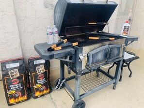 A charcoal grill with two bags of charcoal, two bottles of water, and a bottle of barbecue sauce. - Continental Inn San Diego Hotel Escondido (Escondido)