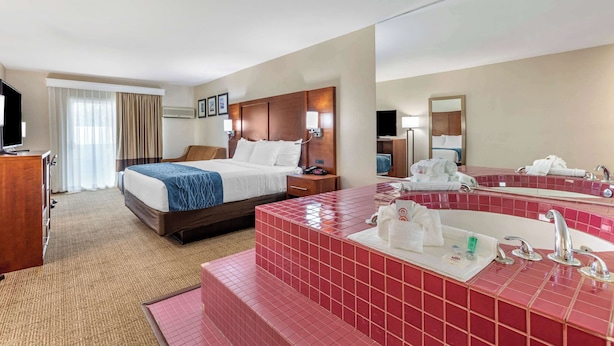 Ein Hotelzimmer mit einem Bett, einem großen Spiegel, einem Badezimmer mit einem roten Fliesenwaschbecken und einem Fernseher.