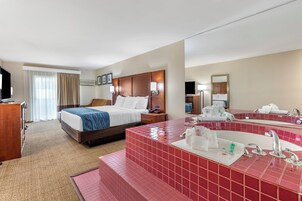 Habitación de hotel con cama, escritorio, televisor y baño con un espejo grande y lavamanos con azulejos rojos.
