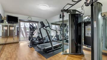 Un gimnasio con máquinas de cardio, una máquina de pesas y un televisor en la pared.