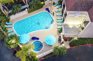 Una piscina con sillas de descanso y sombrillas, rodeada de palmeras y un edificio con el rótulo 'Continental Inn'.