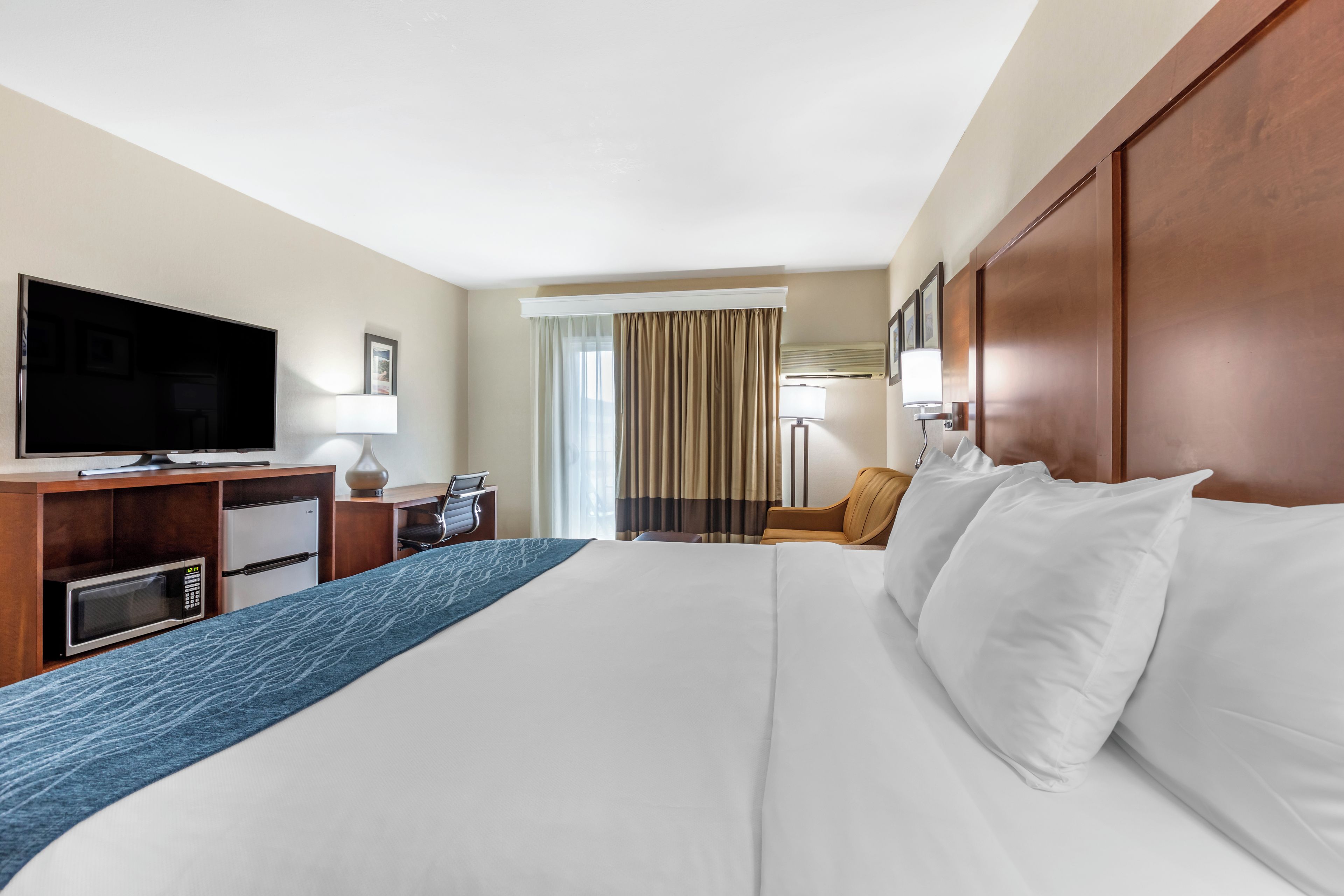 Een hotelkamer met een groot bed, een bureau met een televisie, een magnetron en een stoel.