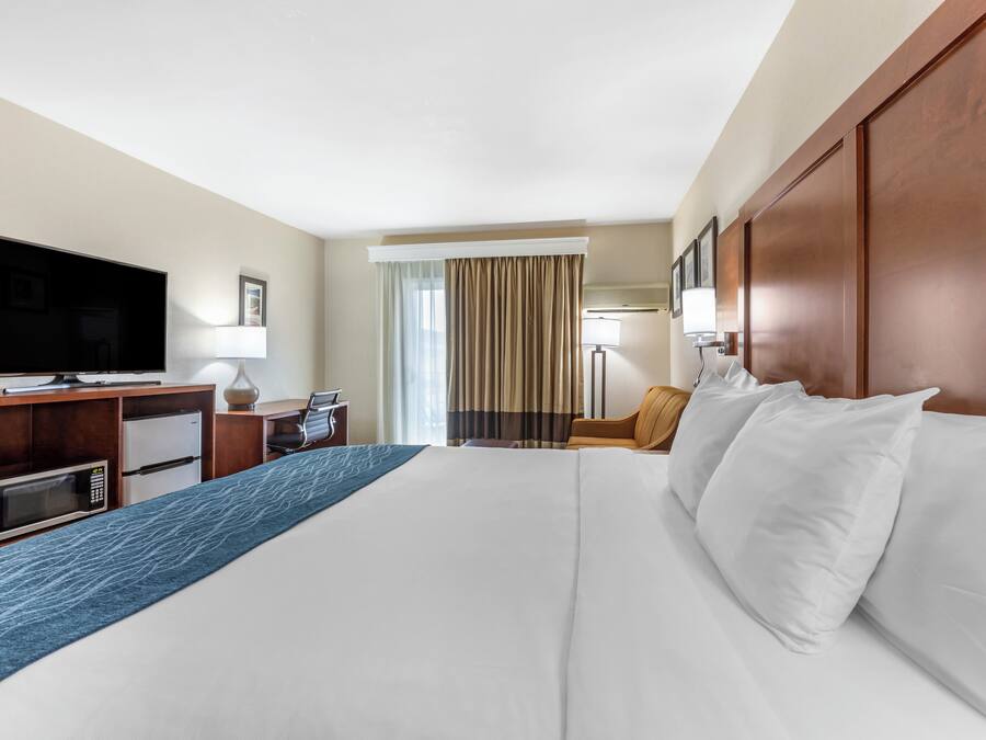 Een hotelkamer met een groot bed, een bureau met een televisie, een magnetron en een stoel.