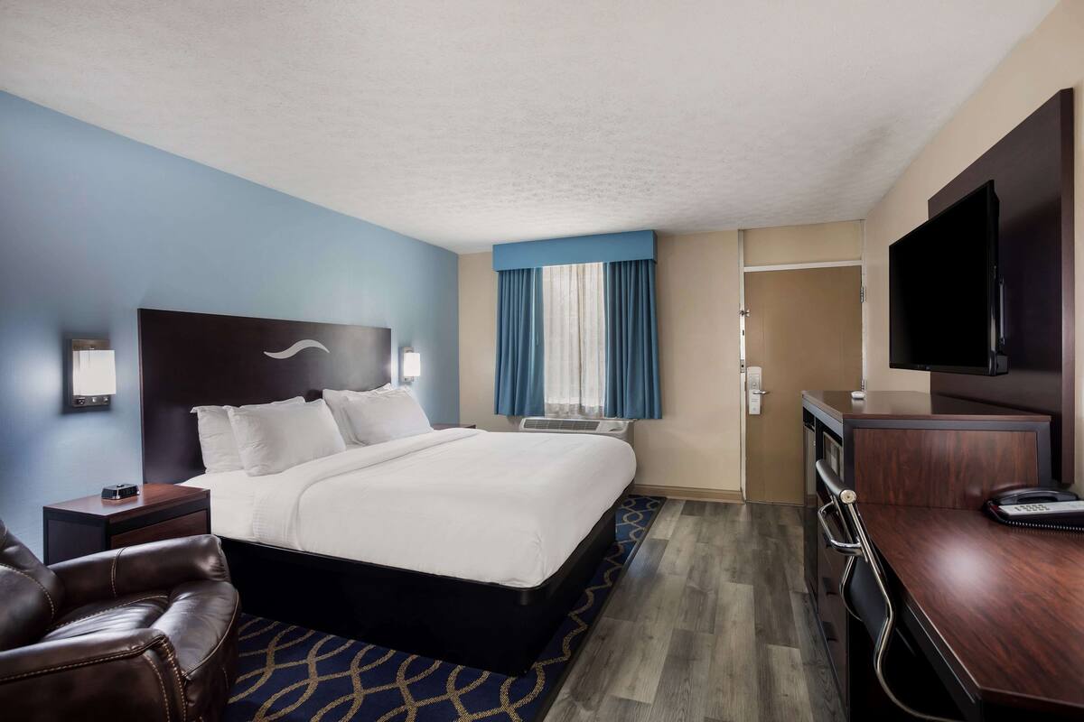 A hotel room with a bed, a desk, a chair, a TV, and a window with curtains.