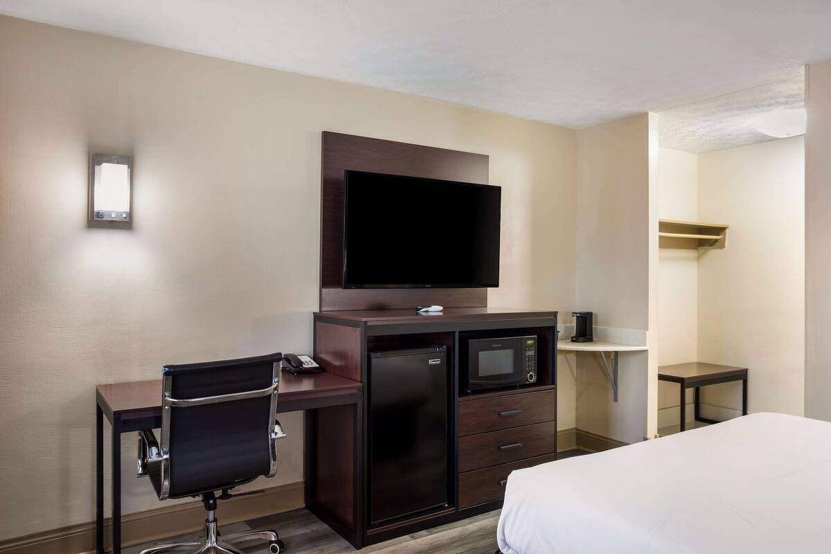 A hotel room with a bed, a desk with a chair, a television, a refrigerator, a microwave, and a small table.