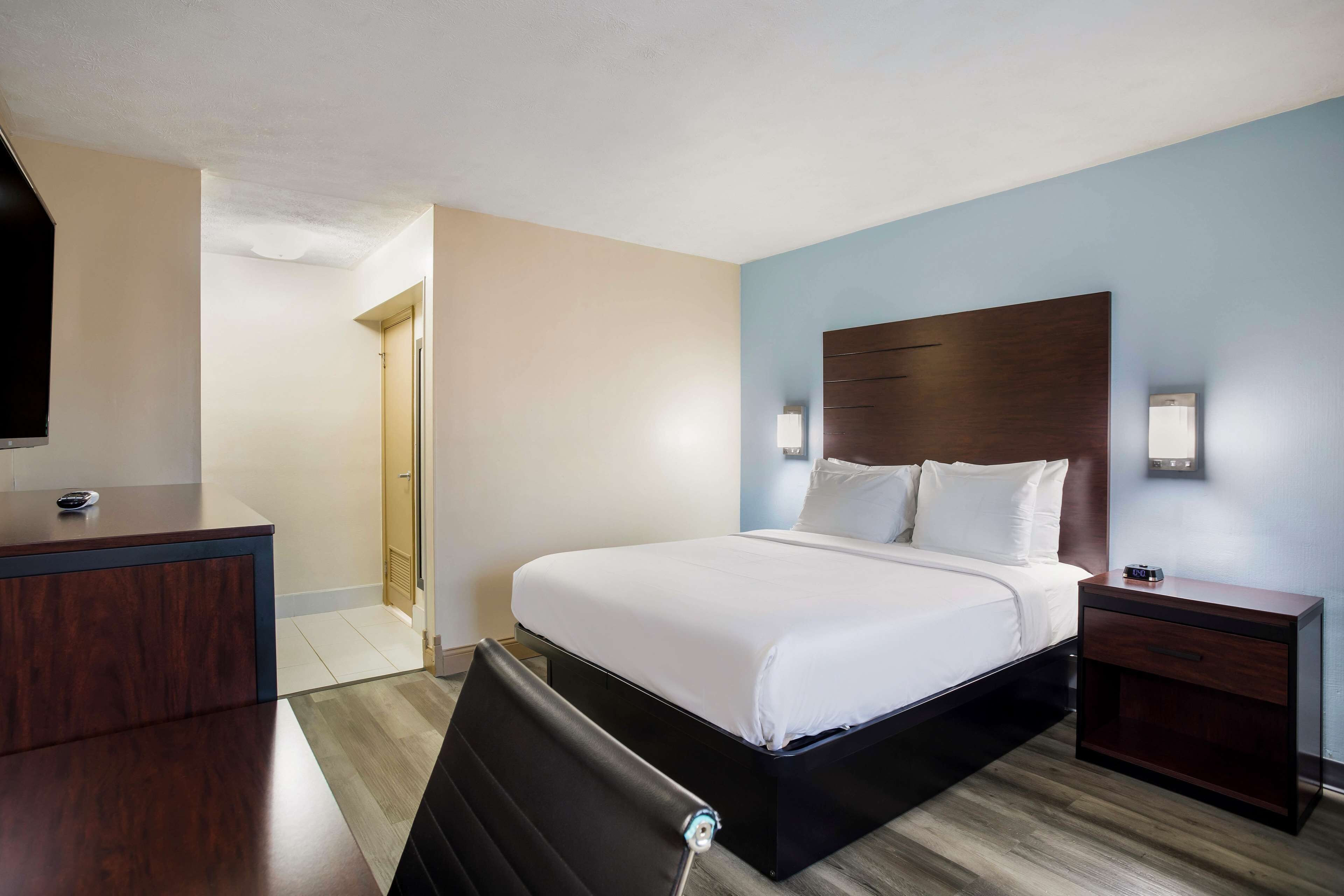 A hotel room with a bed, bedside table, and a desk with a chair.