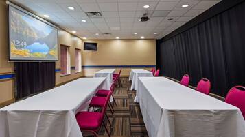 A conference room with white tables and red chairs, a projector screen displaying a landscape, and a clock showing 12:49.