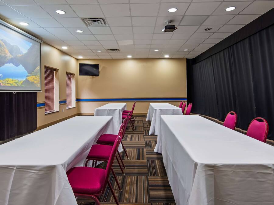 A conference room with white tables and red chairs, a projector screen displaying a landscape, and a clock showing 12:49.