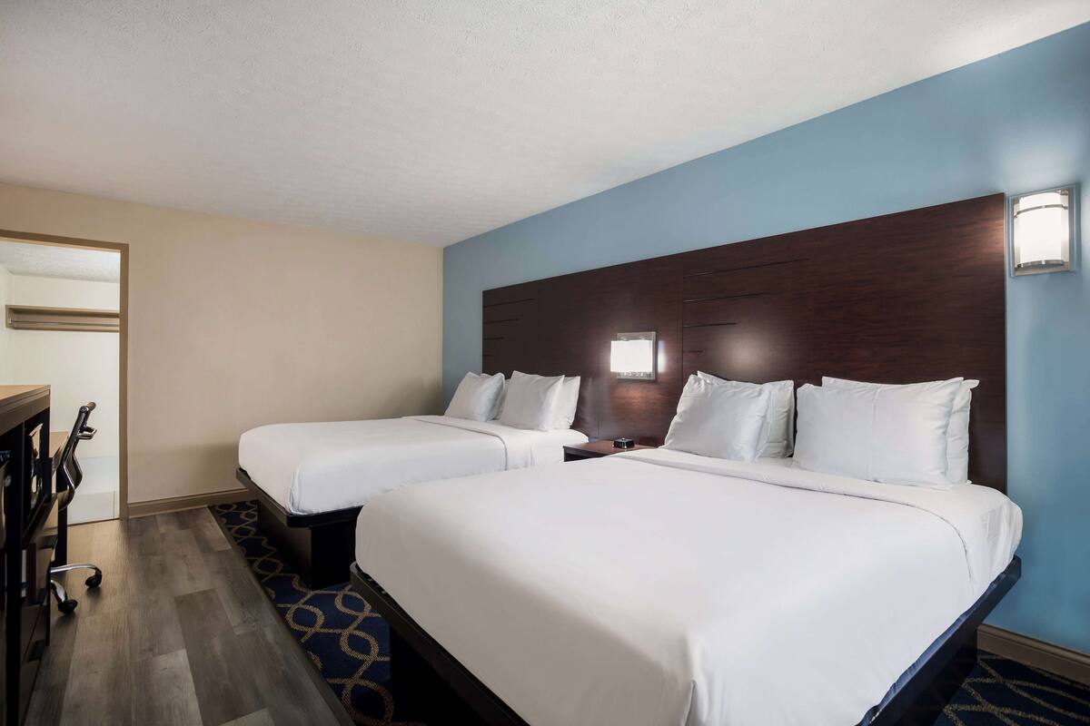 A hotel room with two beds, a desk, and a chair.