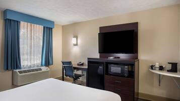 Ein Hotelzimmer mit Bett, Schreibtisch, Stuhl, Klimaanlage, Fernseher, Mikrowelle und einem kleinen Regal mit Gegenständen.