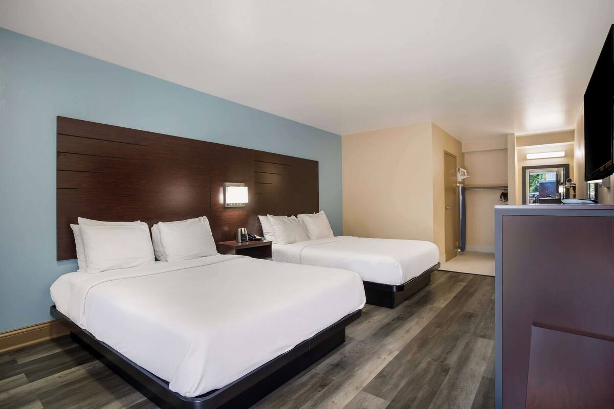 A hotel room with two beds, a wooden headboard, a desk, and a television.