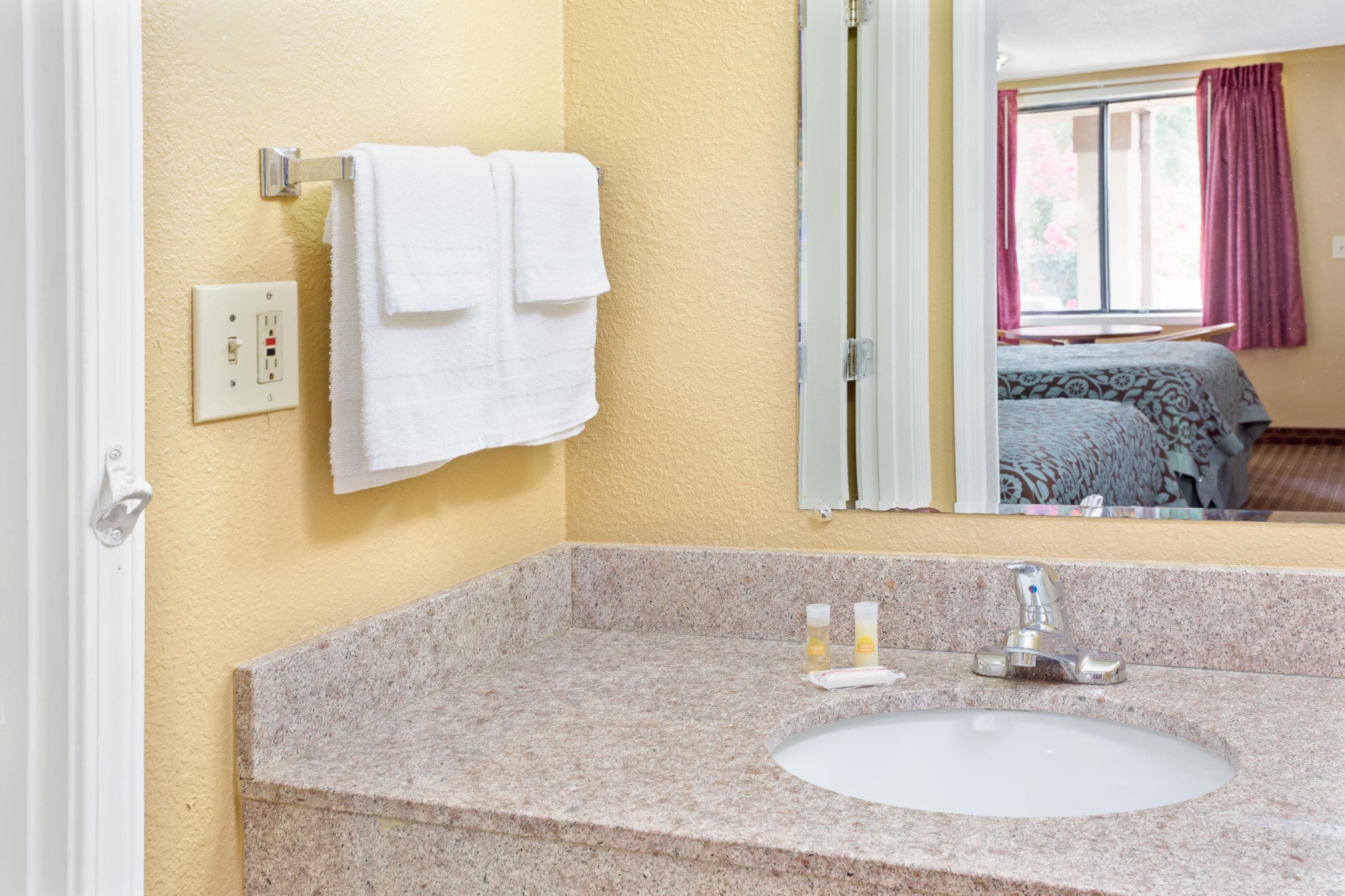 A bathroom with a granite countertop, a sink, a mirror, and a towel rack with two white towels.