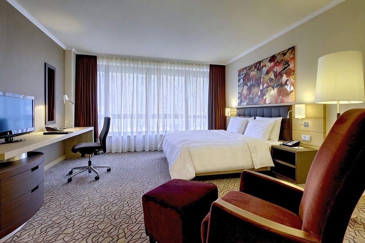 Habitación de hotel con cama, escritorio, silla, televisor y obras de arte en la pared.
