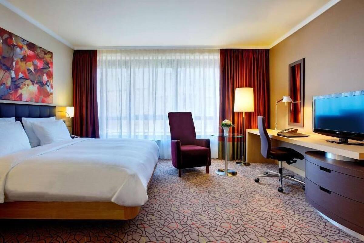 Una habitación de hotel con una cama grande, un escritorio con computadora, una silla y una televisión.