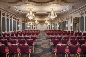 A conference room with rows of red chairs, chandeliers, and ornate wall decorations. - Hilton Mainz (Mainz)